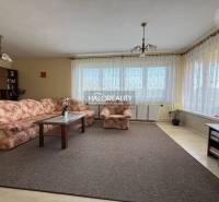 Nappali szőnyeggel, virágmintás kanapéval és fa dekoros padlóval egy családi házban.