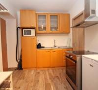 Konyha egy egyszobás lakásban, fa dekor padlóval, világos fa szekrényekkel.