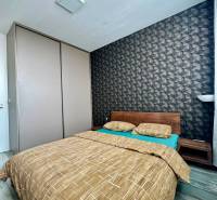 Hálószoba egy kétszobás lakásban ággyal és mintás tapétával, fa dekorációjú padlóval.