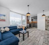 Nappali fa hatású padlóval, kék kanapéval és konyhasarokkal egy kétszobás lakásban.