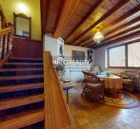 Családi ház belső tere lépcsővel, fa dekorációjú padlóval és rattan bútorokkal.