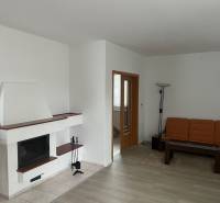 Nappali kandallóval, narancssárga kanapéval, fa mintás padlóval és üvegasztallal.