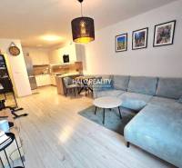 Nappali sarokkanapéval, konyhával és fa dekoros padlóval egy kétszobás lakásban.