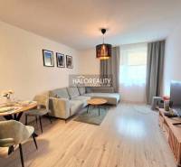 Nappali egy kétszobás lakásban sarokkanapéval és televízióval, fa mintázatú padlóval.