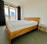 Hálószoba fa ággyal, éjjeliszekrénnyel és erkéllyel egy háromszobás lakásban.