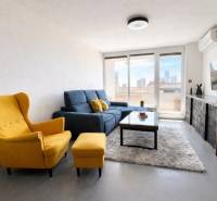 Nappali egy háromszobás lakásban sárga fotellel, kék kanapéval és falra szerelt TV-vel.