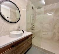 Fürdőszoba fa szekrénnyel, kör alakú tükörrel és zuhanyzóval egy háromszobás lakásban.