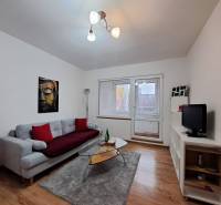 Nappali egy kétszobás lakásban kanapéval, üvegasztallal és fa dekorációjú padlóval.