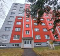 Egy piros homlokzatú lakóház Poprádon, amely előtt járda és fák vannak.