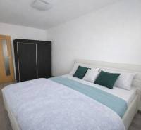 Hálószoba ággyal, beépített szekrénnyel és fa dekorációjú padlóval egy háromszobás lakásban.