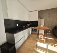 Konyha egy kétszobás lakásban fekete részletekkel és fa dekorációjú padlóval.