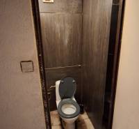 Kerámia burkolatú WC egy háromszobás lakásban, sötét burkolat és szellőzés.