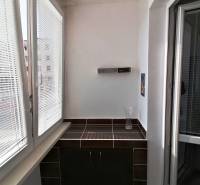 Zasklený balkón v 3-izbovom byte s tmavou dlažbou a skrinkou.