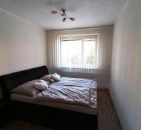 Spálňa s dvojlôžkovou posteľou, závesmi a podlahou s dreveným dekorom v 3-izbovom byte.