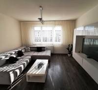 Obývacia izba s pohodlným sedačkou, televízorom a podlahou s dreveným dekorom v 3-izbovom byte.