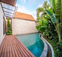 Bali villa medencével, zölddel körülvéve és fa dekorációjú padlóval.