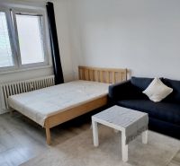 Szoba ággyal, fekete kanapéval és asztallal, fa dekorációjú padlóval.