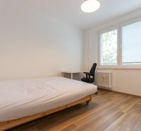 Hálószoba egyszerű ággyal, íróasztallal és fa dekorációjú padlóval egy háromszobás lakásban.