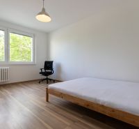 Világos hálószoba egy háromszobás lakásban, fa mintázatú padlóval és nagy ablakokkal.