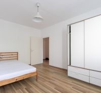 Hálószoba fa ággyal, fehér szekrénnyel és fa mintázatú padlóval egy háromszobás lakásban.