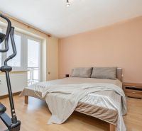Hálószoba ággyal, edzőgéppel és fa mintázatú padlóval egy kétszobás lakásban.