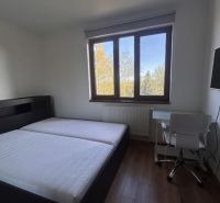 Hálószoba ággyal, asztallal és fa dekorációjú padlóval egy háromszobás lakásban.