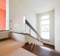 Modern korláttal és szőnyeggel ellátott lépcső egy családi házban, napfényes szoba.