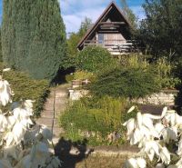Házikó Pozsony-Károlyfalu városrészben, zölddel körülvéve, előtérben fehér virágokkal.