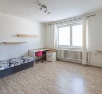 Szoba egy családi házban ággyal, asztallal, rózsaszín székkel és fa dekoros padlóval.
