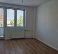 Szoba egy háromszobás lakásban fa dekor padlóval, nagy ablakkal és radiátorral.