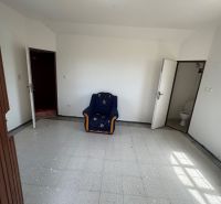 Szoba székkel, fehér falakkal, csempével és WC-be vezető ajtóval a házikóban.