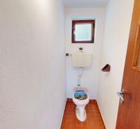 Családi házban lévő WC kerámia padlóval és fa ajtóval.