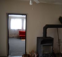 A családi házban van egy mennyezeti ventilátor, egy kályha és egy piros kanapé a háttérben.