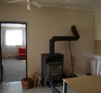 Családi ház belső tere kandallóval, ventilátorral és háttérben piros kanapéval.