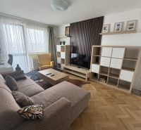 Nappali egy kétszobás lakásban fa mintázatú padlóval, kanapéval és TV szekrénnyel.