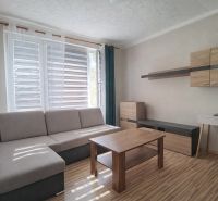 Nappali kanapéval, fa mintázatú padlóval és bútorokkal egy egyszobás lakásban.