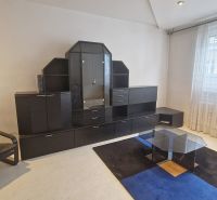 Nappali kanapéval, üvegasztallal és sötét nappali szekrénnyel egy háromszobás lakásban.