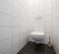 Fehér csempés és fekete padlós WC egy kétszobás lakásban.