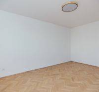 Egy üres szoba fehér falakkal és fa dekorációjú padlóval egy háromszobás lakásban.