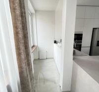 Konyha egy háromszobás lakásban fehér szekrényekkel és márványpadlóval.