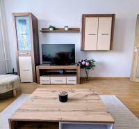 Kétszobás lakás nappalija fa mintázatú padlóval és TV bútorral.