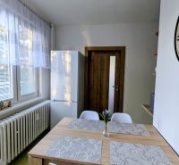 Étkező sarok egy kétszobás lakásban, fa asztallal és fehér székekkel.