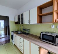 Konyha egy kétszobás lakásban mikrohullámú sütővel és főzőlappal, egy másik helyiség felé nézve.