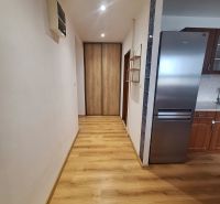 Előszoba beépített szekrénnyel és konyhával egy 2 szobás lakásban, fa padló, világos falak.