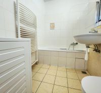 Fürdőszoba egy kétszobás lakásban káddal, mosdóval és mosógéppel, fehér csempével burkolva.