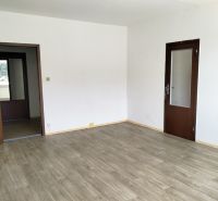 Tágas szoba egy háromszobás lakásban, fa dekorációjú padlóval és fehér falakkal.