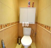 Bézs csempékkel és fali szekrénnyel ellátott WC egy háromszobás lakásban.
