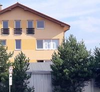 Sárga ház ferde tetővel és ablakokkal a fák mögött, közel az irodai vonalakhoz.