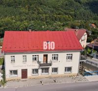 Egy épület Bélen piros tetővel, zölddel körülvéve és előtte úttal.