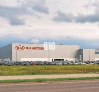Kia Motors épülete Zsolnán, kereskedelmi telkek parkoló autókkal és füves területtel.